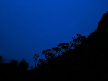 Low angle view of silhouette trees against clear blue sky