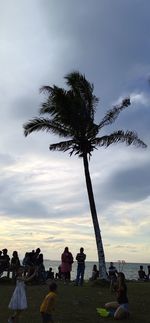 People sitting on palm tree against sky during sunset