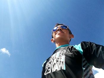 Low angle view of boy wearing sunglasses against clear blue sky