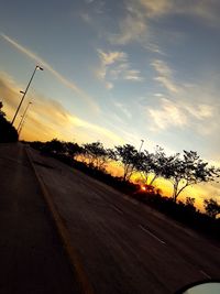 Road by trees against sky during sunset