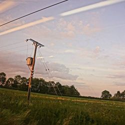 Electricity pylon on field against cloudy sky