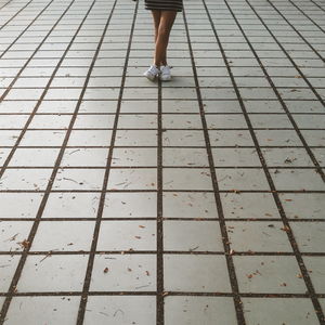 Low section of woman with legs crossed at ankle while standing on walkway