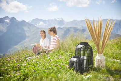 Women sitting on grass by mountain