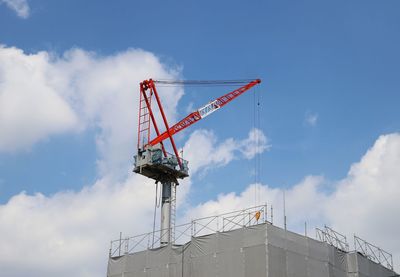 Low angle view of crane against building against sky