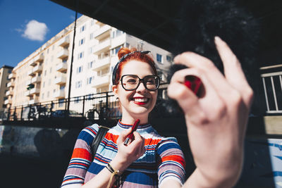 Young woman looking at mobile phone while applying lipstick in city