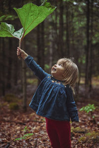 Beautiful baby is hiding in the forest from the rain under the burdock