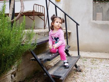 Full length of cute girl on pink while sitting on staircase