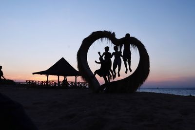 Silhouette people at beach against sky during sunset