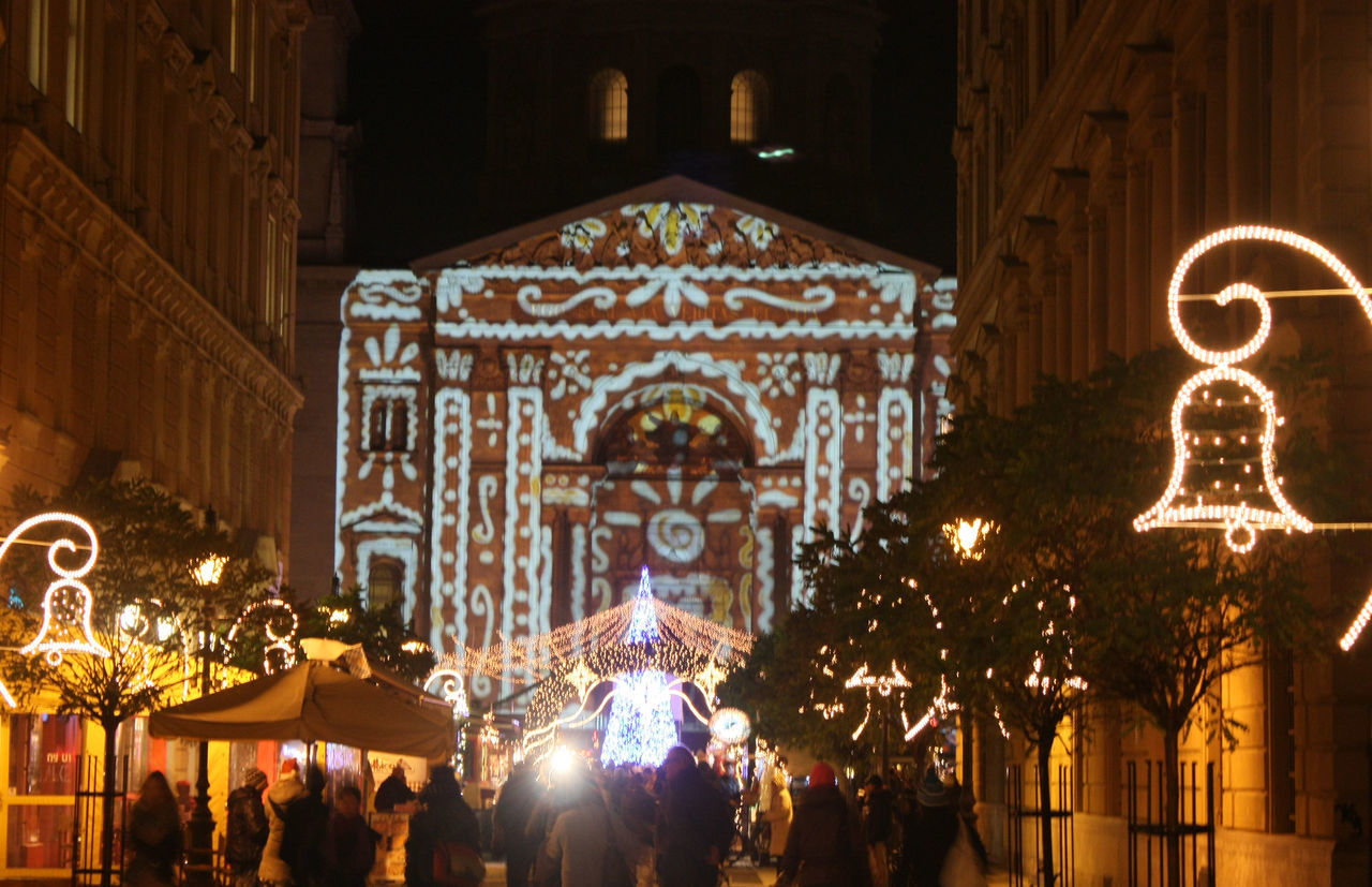 GROUP OF PEOPLE AT ILLUMINATED TEMPLE AGAINST BUILDING AT NIGHT