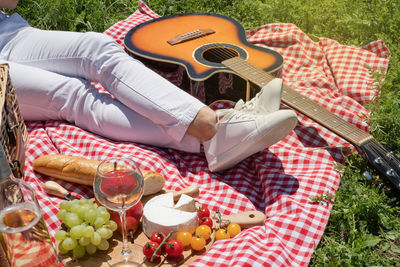 Unrecognizable young woman in white pants outside having picnic, eating and playing guitar. 