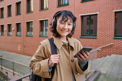 Portrait of young woman standing against building