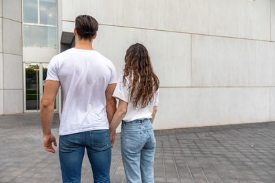 Rear view of couple holding hands while looking at building in city