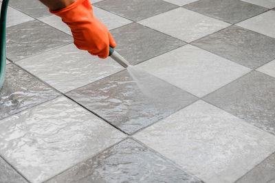 Cropped hand of man spraying water on footpath with hose