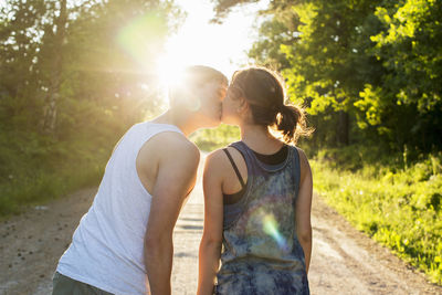 Rear view of couple kissing on dirt road against bright sun