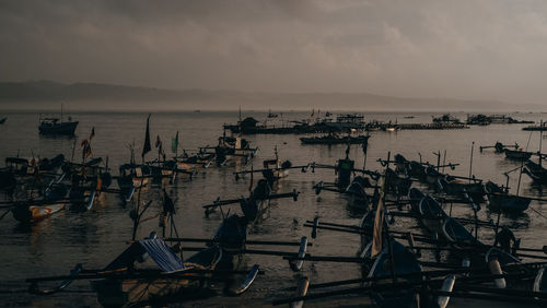 Fishing boats moored at harbor against sky