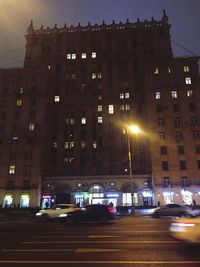 Cars on illuminated road by buildings in city at night