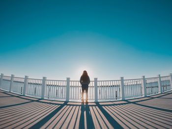 Rear view of woman standing on railing against blue sky