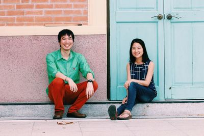 Portrait of smiling friends sitting against house