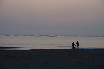 People standing on beach against sky during sunset