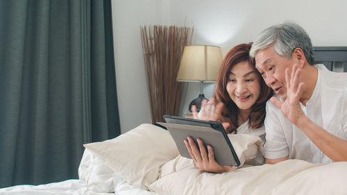 Happy woman using mobile phone while sitting on bed at home