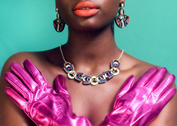 Midsection of woman with arms covering chest wearing shiny pink gloves and statement jewellery 