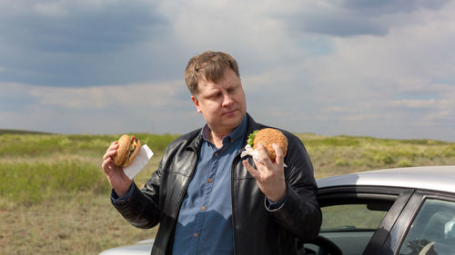 Hungry man in the fresh air makes a choice between two burgers.