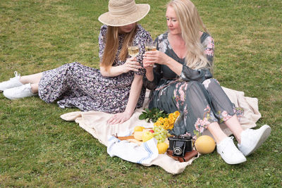 Two young women in a summer long dresses is resting on a picnic,blanket on grass