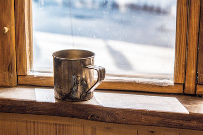 Old metal mug stands on a wooden window sill