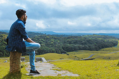 Side view of young man looking at landscape against sky