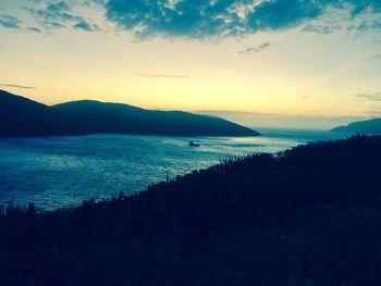 Scenic view of river by silhouette mountains against sky during sunset