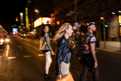 Group of stylish multiracial friends walking together on city street for party at night