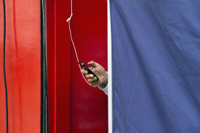 Cropped hand of person using phone behind curtain at home