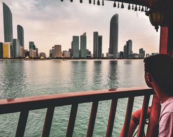 Man standing by railing on river against buildings in city