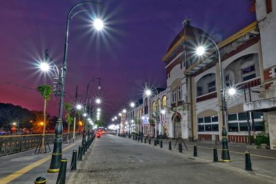 Empty road along illuminated buildings at night