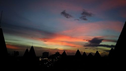 Silhouette of city against cloudy sky during sunset