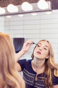 Young woman applying mascara in front of bathroom mirror