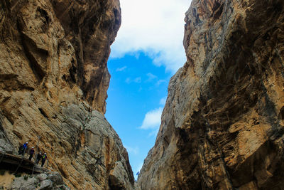 Low angle view of people standing amidst rocky mountains against sky