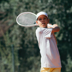 Smiling boy looking away while holding tennis racket