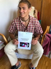 Smiling young man holding spiral book while sitting at home