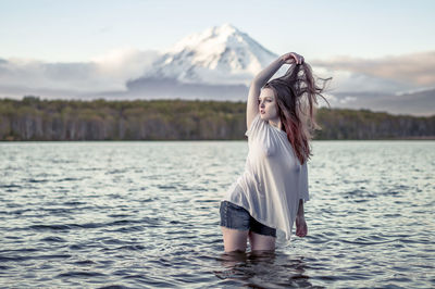 Young woman looking away while standing in lake against sky during sunset