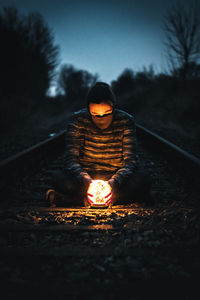 Man with illuminated lighting equipment sitting on railroad tracks during dusk