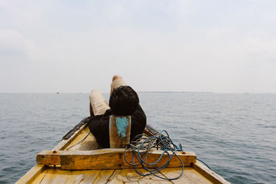 Man lying on boat in sea against sky