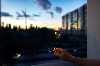 Close-up of woman hand holding city against sky during sunset