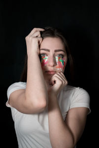 Close-up portrait of sad young woman with face paint against black background