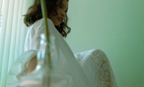 Side view of young woman sitting on white wall