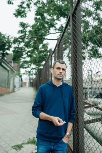 Portrait of young man standing against fence