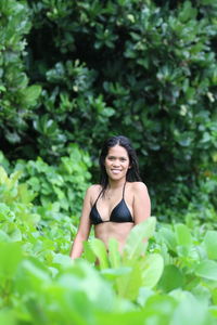 Portrait of smiling young woman in bikini standing amidst plants