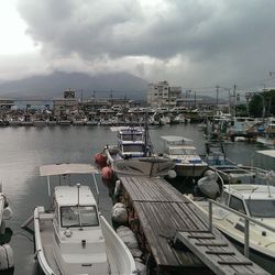 Boats moored at harbor against cloudy sky