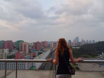 Rear view of woman looking at cityscape against cloudy sky