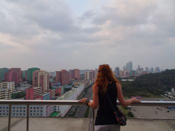 Rear view of woman looking at cityscape against sky